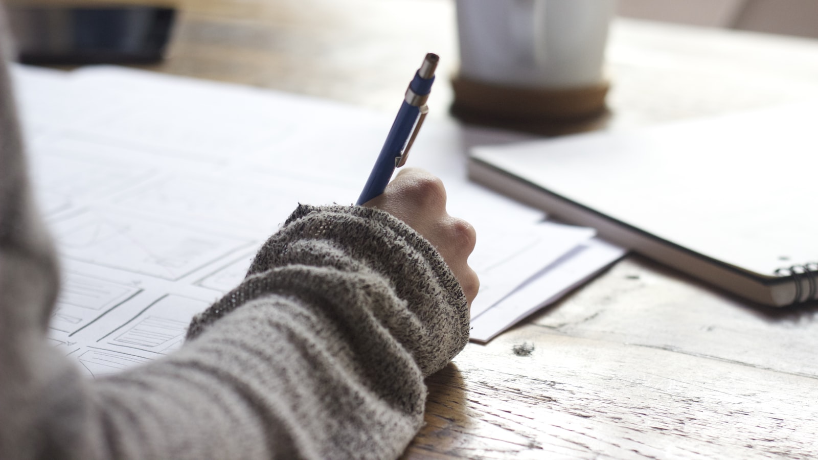 An open paper planner with a pen resting on a wooden desk in soft natural light