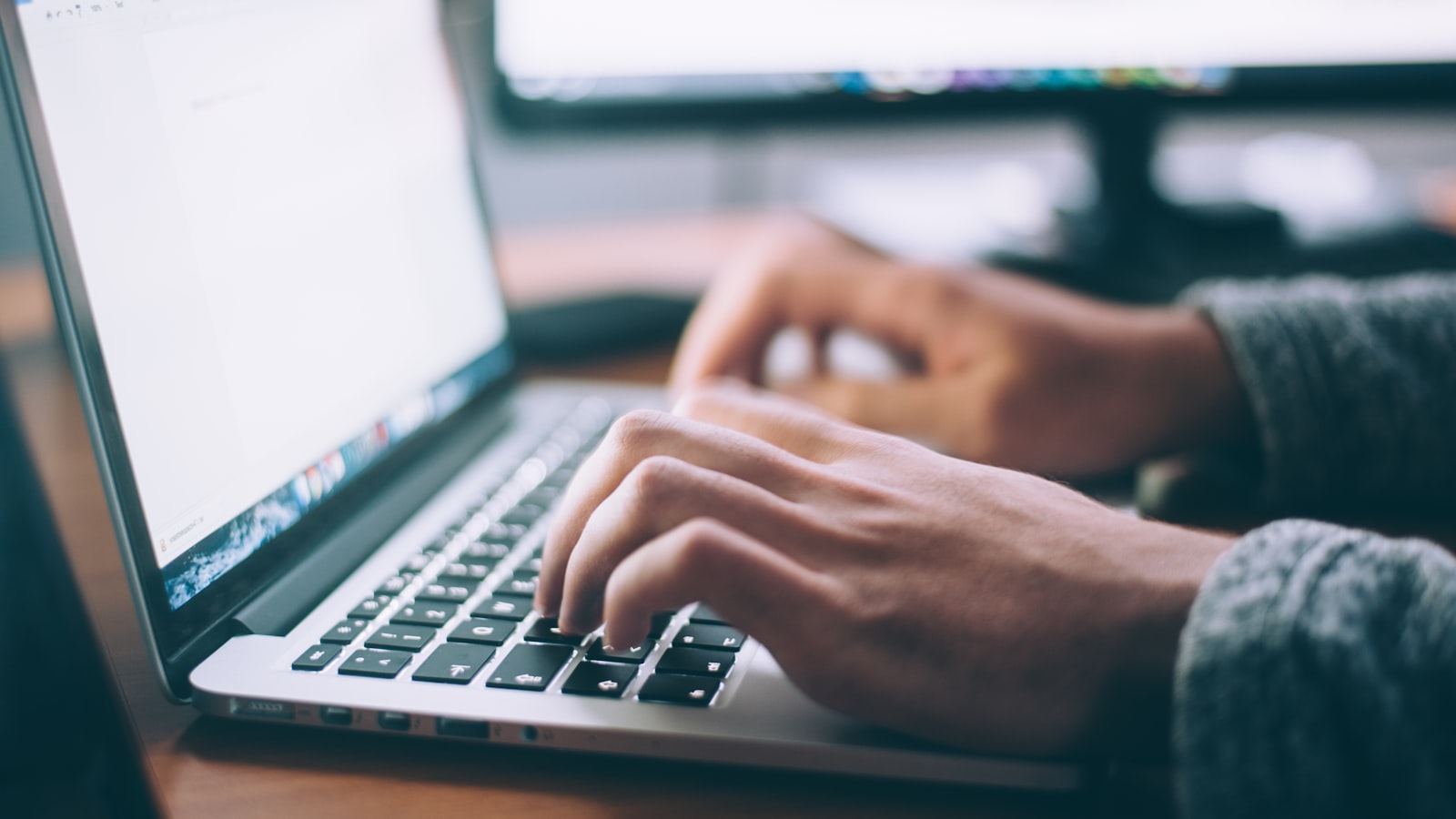 A laptop and a notebook on a clean desk in a quiet, sunlit room with no clutter.