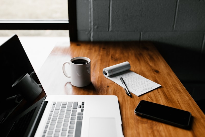 An open notebook and a cup of coffee on a wooden desk by a window in soft morning light.